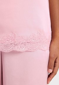 Pink clothing featuring a delicate lace trim at the bottom, showcasing floral patterns and scalloped edges on smooth fabric.