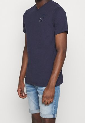 Marineblå v-hals t-shirt lavet af bomuld, med korte ærmer og et lille hvidt grafisk print på venstre brystområde.