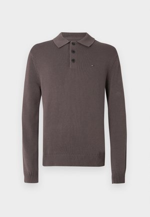 Bruine polo van gebreide stof met lange mouwen, voorzien van een geribde kraag, manchetten en zoom, afgewerkt met drie knopen en een klein vlaglogo op de linkerborst.