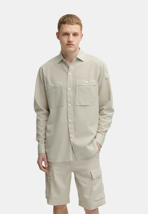 Camicia beige a maniche lunghe con due tasche sul petto e chiusura a bottoni, abbinata a pantaloni cargo beige con tasche laterali e taglio dritto.