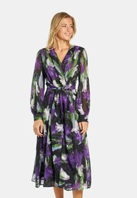 Langes, gemustertes Kleid mit schwarzem Grund und großen lila und grünen Blumenmustern. Es hat lange Ärmel und eine taillierte Bindung.