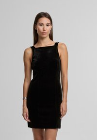 Černé sametové šaty se střihem s rovním výstřihem, úzkým střihem a širokými ramínky. Tkanina má hladký, jemný povrch.