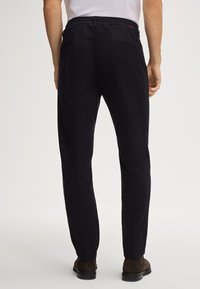 Ciemnogranatowe spodnie z elastycznym pasem, zwężanymi nogawkami i dwoma tylnymi kieszeniami. Materiał wydaje się lekki o gładkiej fakturze.