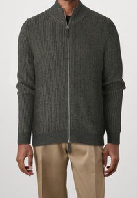 Tummanharmaa vetoketjullinen neulepaita, jossa on ribbikuvioitu pinta, korkea kaulus ja kaksi sivutaskua. Pehmeä kangas ja istuvat pitkät hihat.