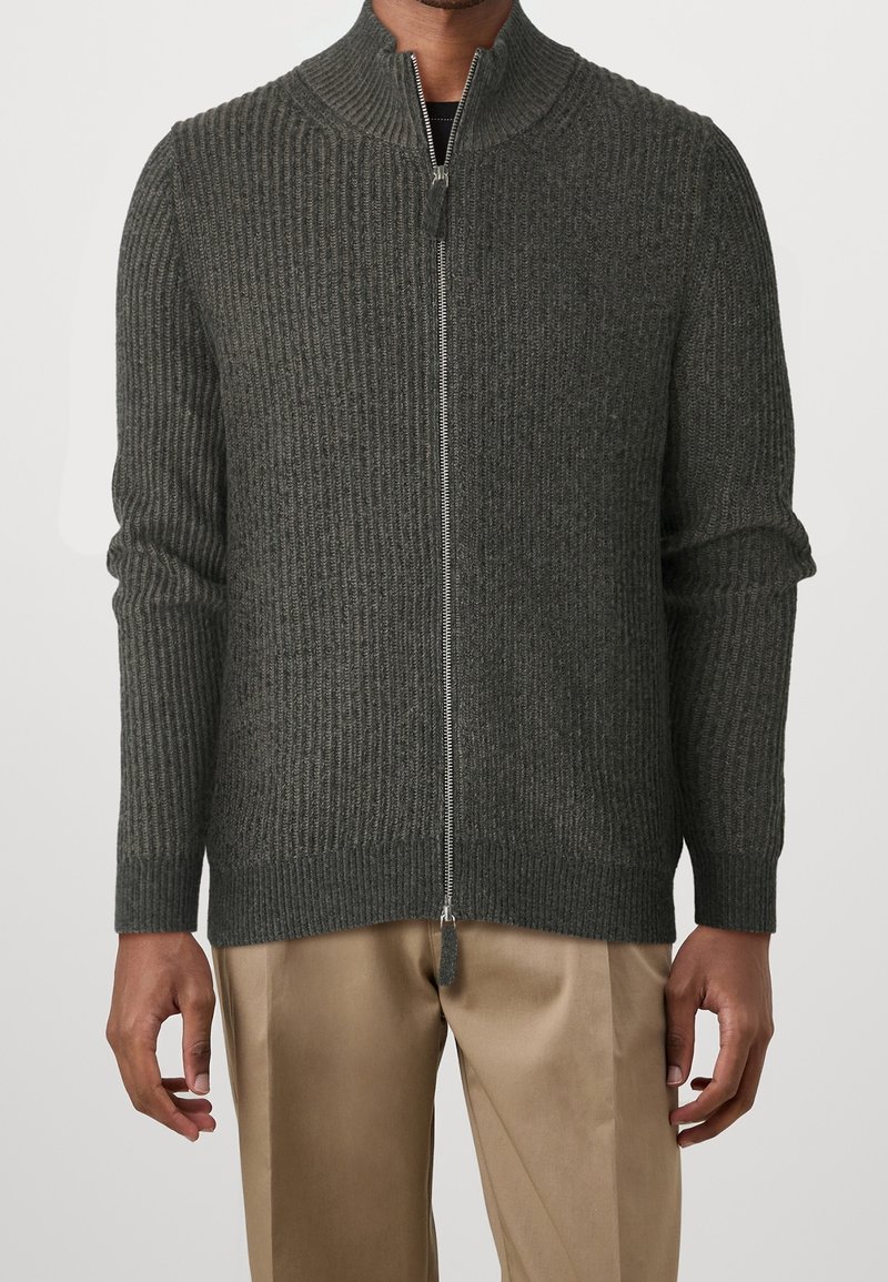 Tummanharmaa vetoketjullinen neulepaita, jossa on ribbikuvioitu pinta, korkea kaulus ja kaksi sivutaskua. Pehmeä kangas ja istuvat pitkät hihat.