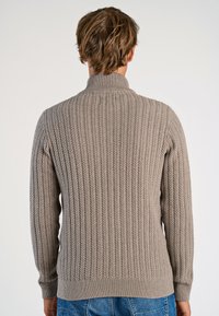 Kabelstickad tröja i ljus taupe, med hög krage, ribbade manschetter och nederkant, samt mönster med textur genom hela ryggen.