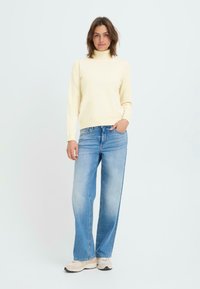 Crèmekleurige coltrui, lichtblauwe wijduitlopende jeans en beige sneakers. Zachte textuur, relaxte pasvorm, minimaal patroon.