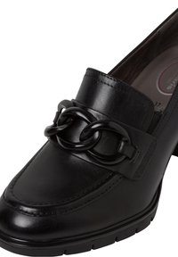 Mocassin en cuir noir avec un détail de chaîne épaisse sur le dessus du pied et un petit talon bloc, avec des bords cousus et une semelle en caoutchouc.