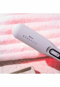 Appareil de beauté StyLPro blanc avec boutons de puissance et de mode reposant sur une serviette rose et un plan de travail tacheté.