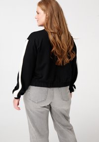 Sweatshirt noir cropped avec des rayures blanches sur les côtés, poignets et taille côtelés, associé à un pantalon en denim taille haute gris clair.