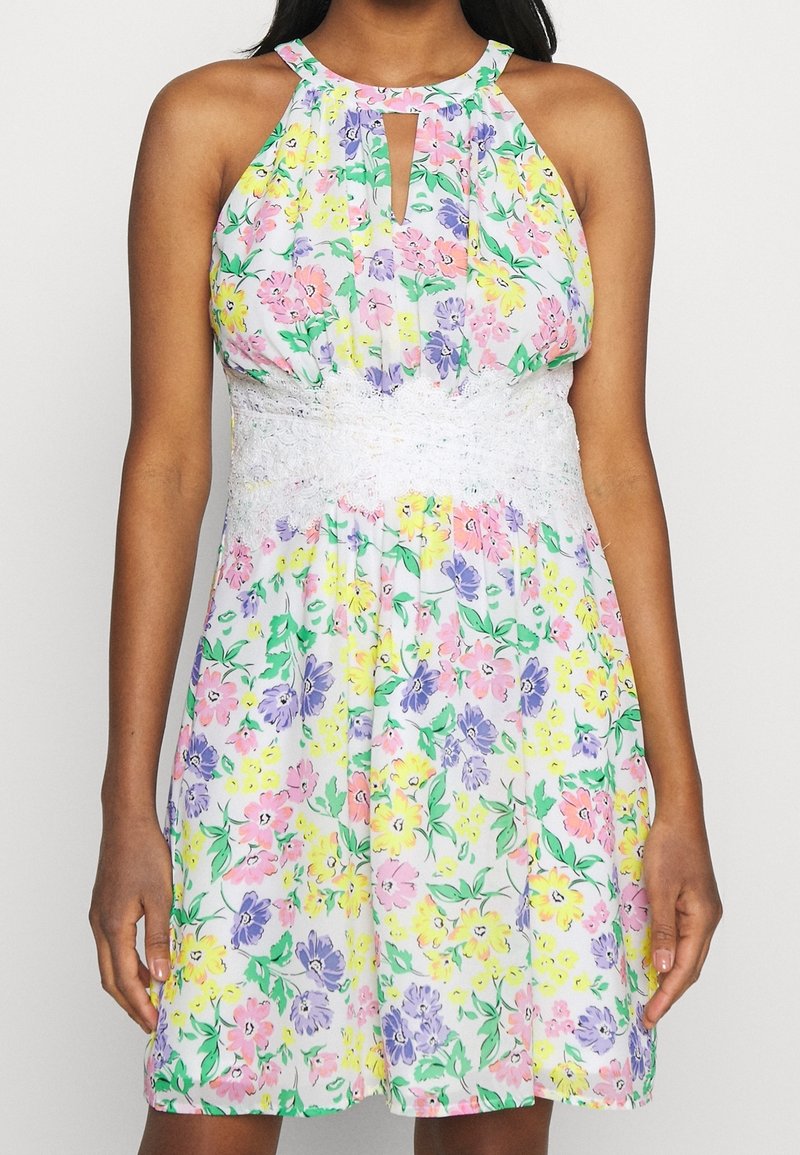 Robe fleurie avec une ceinture en dentelle blanche, présentant un col licou et une découpe en forme de goutte. Les couleurs incluent le rose, le jaune et le violet.