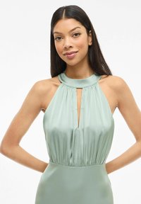 Sukienka na szyję z miękkiego, zielonego satyny z plisowanym zdobieniem na biuście i wycięciem typu keyhole, z dopasowaną talią i lejącym się dołem.