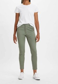 Olivgröna, tapered jeans i bomull med femfickorsdesign och knappstängning. Kombineras med en enkel vit T-shirt och sneakers.