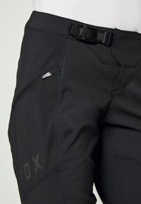 Zwarte performancebroeken van gestructureerde stof, voorzien van een zijzak met rits, een verstelbare taillegesp en contrasterende stikdetails.