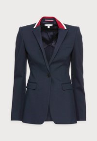 Granatowa marynarka na miarę o dopasowanym kroju, zapinana na jeden guzik, z kontrastowymi czerwonymi i białymi akcentami na kołnierzu. Dwie przednie kieszenie, gładka faktura.