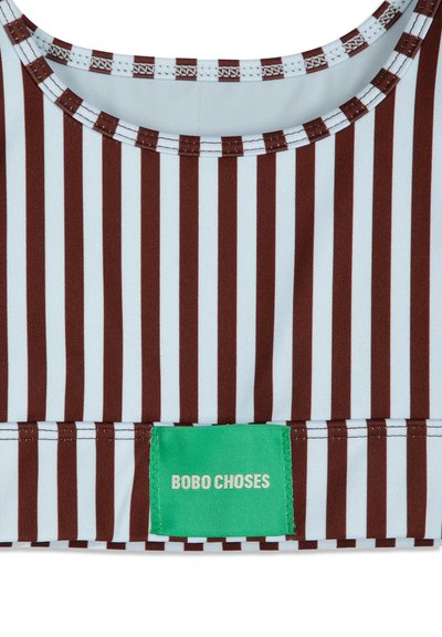 Gros plan d'un tissu rayé verticalement marron et blanc avec une étiquette verte indiquant "BOBO CHOSES", cousue près du bord inférieur.