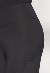 Sorte leggings med høj talje, glat tekstur og en sidelomme med flade sømme for et strømlinet udseende.