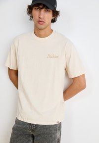 Beez puuvillane T-särk lühikeste varrukatega, millel on vasakul rinnal väike, heledat pruunikat "Dickies" logo. Sobitatud hallide teksadega.