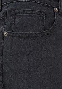 Vaqueros de mezclilla negra con un diseño clásico de cinco bolsillos, herrajes en tono plateado y un acabado suave y texturizado. La vista en primer plano se centra en el bolsillo trasero.