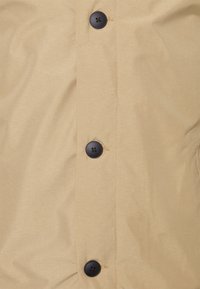 Beige button-up jacket with a smooth texture, featuring black buttons and visible stitching along the front placket.