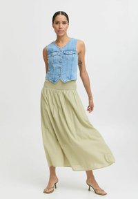 Veste en denim bleu clair avec un col en V, cinq boutons et deux poches avant, associée à une jupe fluide de longueur cheville olive.