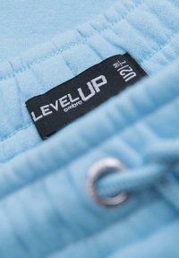 Světlomodrá tkanina s texturovaným povrchem, s černou nálepkou s nápisem „LEVEL UP“ a stříbrným okem s šňůrkou.