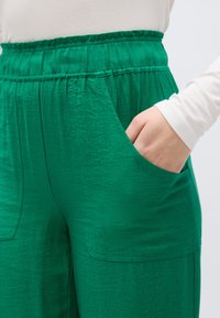 Πράσινο παντελόνι από υφασμάτινη ύλη με υφή, με ελαστική μέση και πλαϊνές τσέπες. Διαθέτει άνετη εφαρμογή με ορατές ραφές.