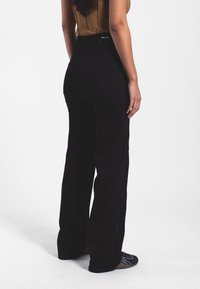 Pantalones de mezclilla negros de cintura alta, diseño de pierna recta y bolsillos traseros. La tela tiene una textura suave y un hardware mínimo.