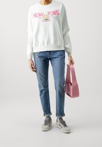 Felpa bianca con interno in pile e scritta "NEW YORK" in rosa, jeans blu, sneakers grigie e borsa rosa con un design strutturato.