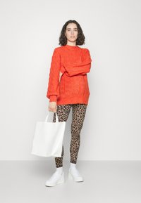 Narančasti pleteni pulover s uzorkom pletenice, upareni s smešastim tajicama s leopard uzorkom. Bijela torba i bijele platforme tenisice.
