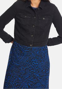 Svart denimjacka i kort modell med två bröstfickor, knappfram, och silverfärgad hårdvara, kombinerad med en blåmönstrad klänning.