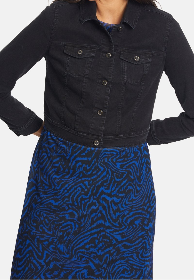 Svart denimjacka i kort modell med två bröstfickor, knappfram, och silverfärgad hårdvara, kombinerad med en blåmönstrad klänning.