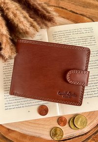 Brown leather wallet with a smooth texture, stitched edges, and a snap closure, featuring "Gusti Leder studio" embossed on the surface.