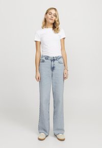 Jeans azzurri a vita alta con gamba dritta e dettagli sbiaditi, abbinati a una maglietta fitted bianca a maniche corte e calzature beige.