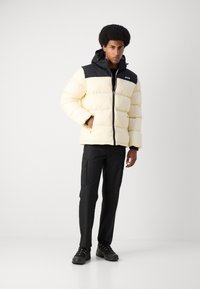Giacca imbottita gialla chiaro con spalle nere, chiusura a zip e cappuccio. Pantaloni cargo neri e sneaker nere completano l'outfit.