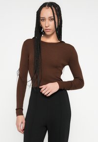Hnedý rebrovaný dlhý rukáv s okrúhlym výstrihom, priliehavým strihom a detailmi z textúrovaného textilu v páre s čiernymi vysokými nohavicami.