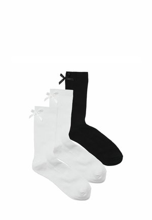 Zwei Paar Baumwollsocken: ein Paar weiß mit einer weißen Schleife, ein Paar schwarz mit einer schwarzen Schleife. Beide verfügen über eine gerippte Textur und ein Standard-Crew-Längen-Design.