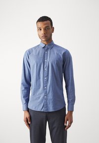Camisa de botones en azul claro con un sutil patrón geométrico, mangas largas y cuello estándar. Textura suave con cierre de botones en la parte frontal.
