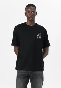 Black cotton t-shirt with a crew neck, short sleeves, and a graphic pocket detail featuring the word "BOSS." Worn with dark gray jeans.