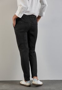 Svarta tapered byxor med elastisk midja, bakfickor och en mjuk yta, tillsammans med vita avslappnade sneakers.