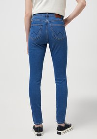 Jeans skinny azules de cintura alta, con bolsillos traseros con costura en zigzag y una etiqueta de cuero marrón en la cintura.