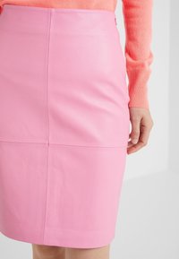 Gonna a tubino in pelle rosa con una texture liscia, caratterizzata da dettagli cuciti e una zip laterale. Il tessuto ha una leggera lucentezza.