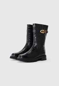Botas negras hasta la rodilla hechas de cuero con textura de cocodrilo, con una suela de goma resistente y detalles en tono dorado en el costado.