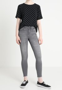 Haut noir à manches courtes avec des pois bleus, associé à un jean skinny gris avec des détails usés, et des baskets noires.