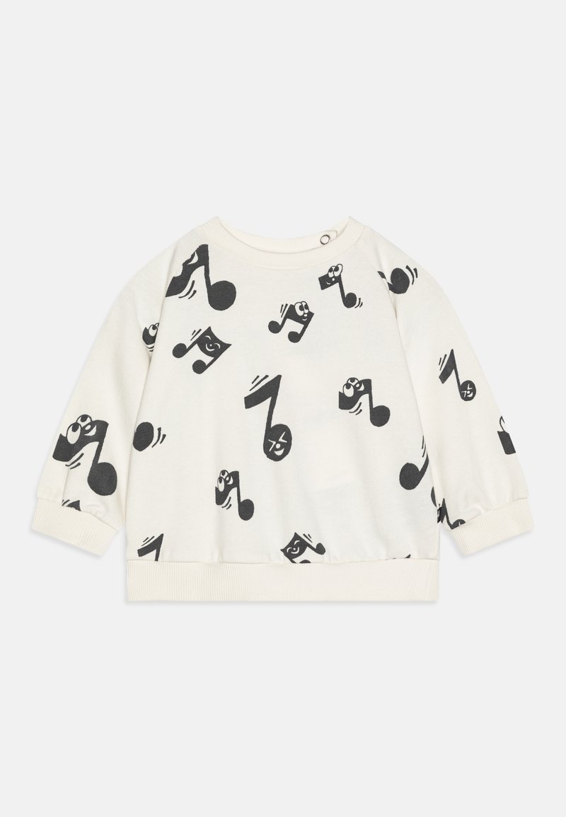 Pull en laine crème à manches longues pour bébé, avec des notes de musique noires et des visages de dessins animés souriants imprimés partout.