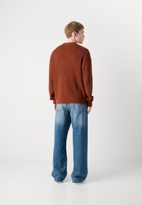 Bruin geribbeld sweater met verlaagde schouders en lange mouwen, gecombineerd met lichtblauwe wijde jeans met een vervaagde afwerking en achterzakken.