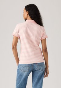 Polo a maniche corte di colore rosa chiaro con righe bianche, dotato di colletto e design aderente, abbinato a jeans blu a vestibilità ampia.