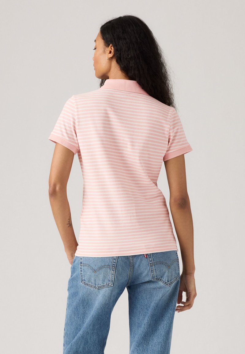 Kurzarm-Poloshirt in Hellrosa mit weißen Streifen, ausgestattet mit einem Kragen und einem figurbetonten Schnitt, kombiniert mit blauen, lässigen Jeans.