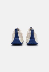 Baskets de sport beige clair avec des accents bleus, présentant une semelle texturée, un col rembourré et un logo sur le talon.