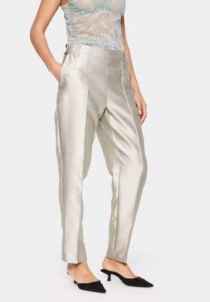 Pantalones de satén plateado con una textura suave, corte entallado y costuras laterales. Combinados con tacones negros de punta afinada.